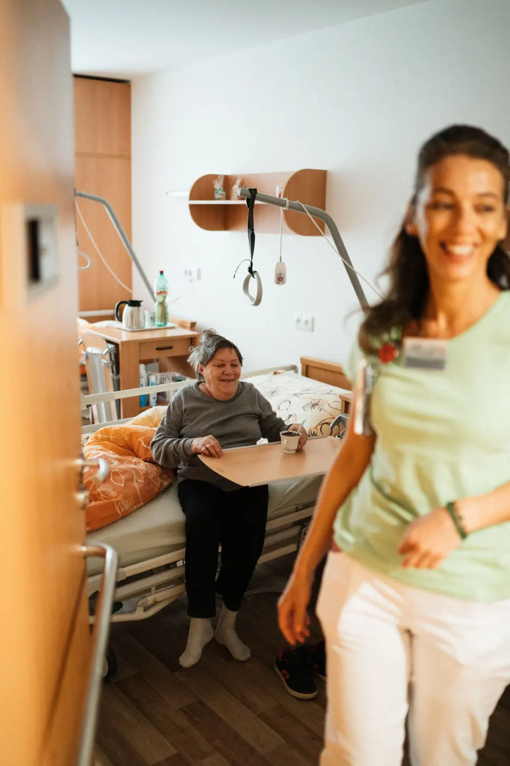 Une soignante souriante dans la chambre d'une résidente âgée, elle aussi souriante